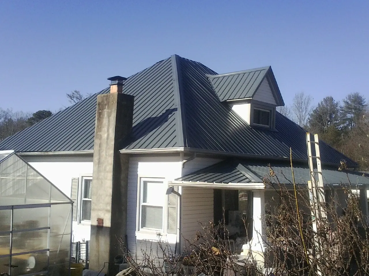 Dark blue standing seam metal roof on a white farmhouse with dormer — Slate & Tile Roof Repair by Roofing Brothers in Chippewa Falls