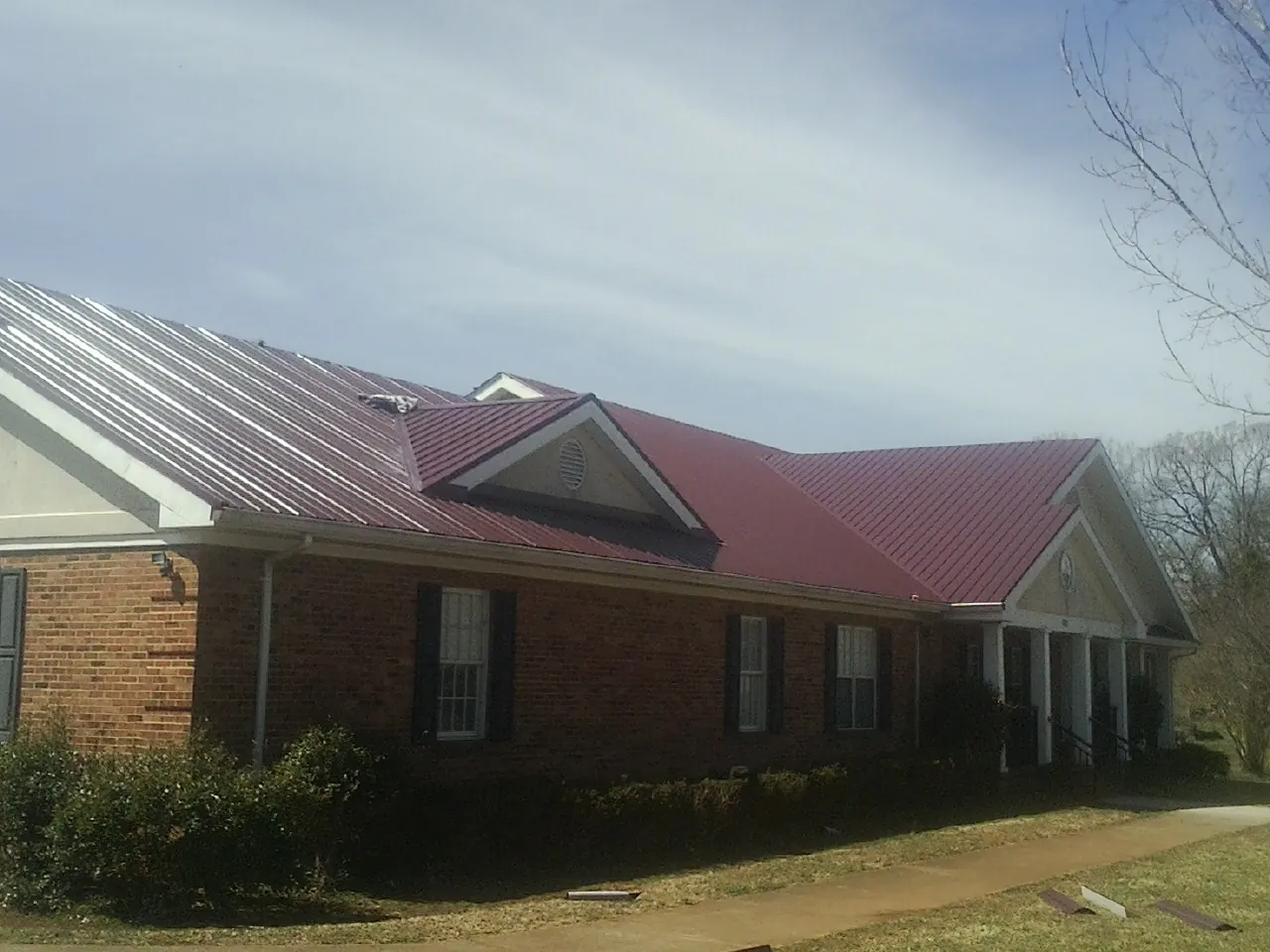 Red metal roof with gabled entries on a long brick building, from a Hail Damage Roof Repair job in Chippewa Falls