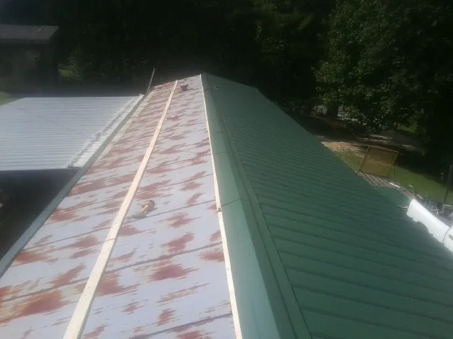 Old rusted panels beside newly installed green metal roofing — Wind Damage Roof Repair by Roofing Brothers in Chippewa Falls