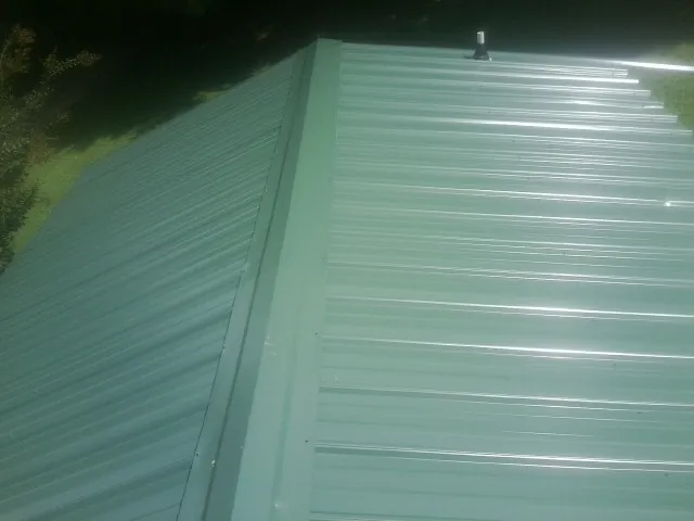 New green metal panels meeting at the ridge of a roof — Flat Roof Repair work by our crew in Chippewa Falls