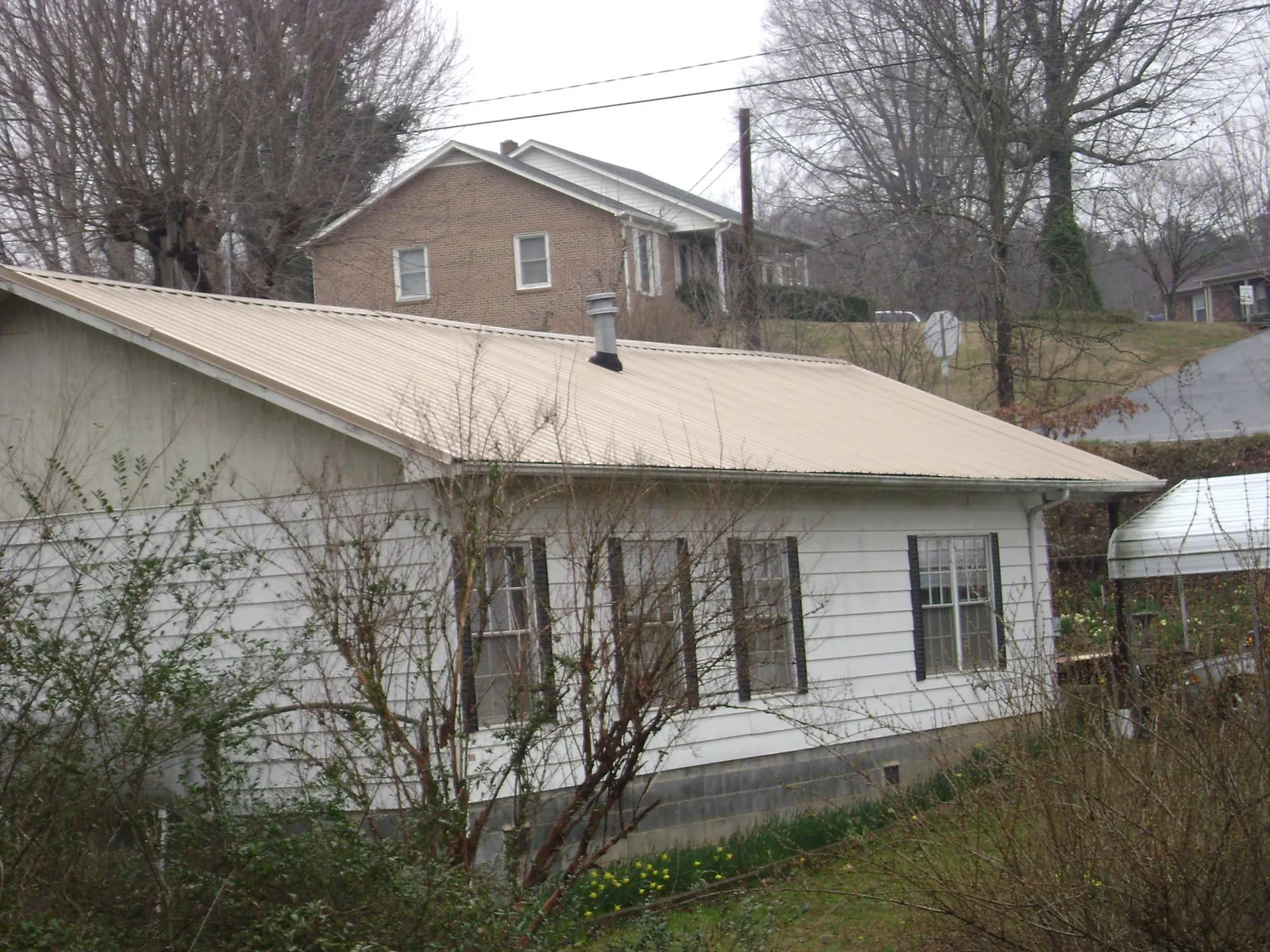 Tan metal roof on a white sided house set into a hillside — Commercial Roofing by Roofing Brothers in Chippewa Falls