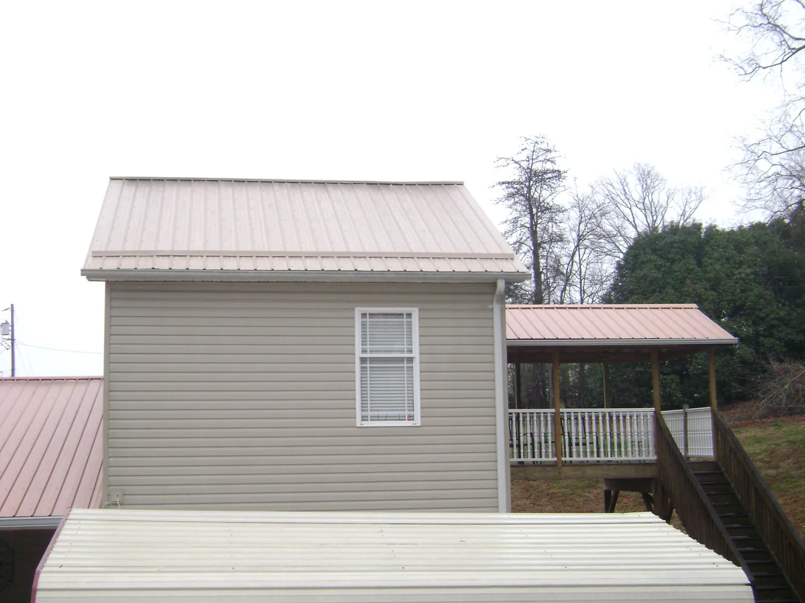 Tan metal roofs on a two story addition and attached porch, from a Roof Replacement job in Chippewa Falls