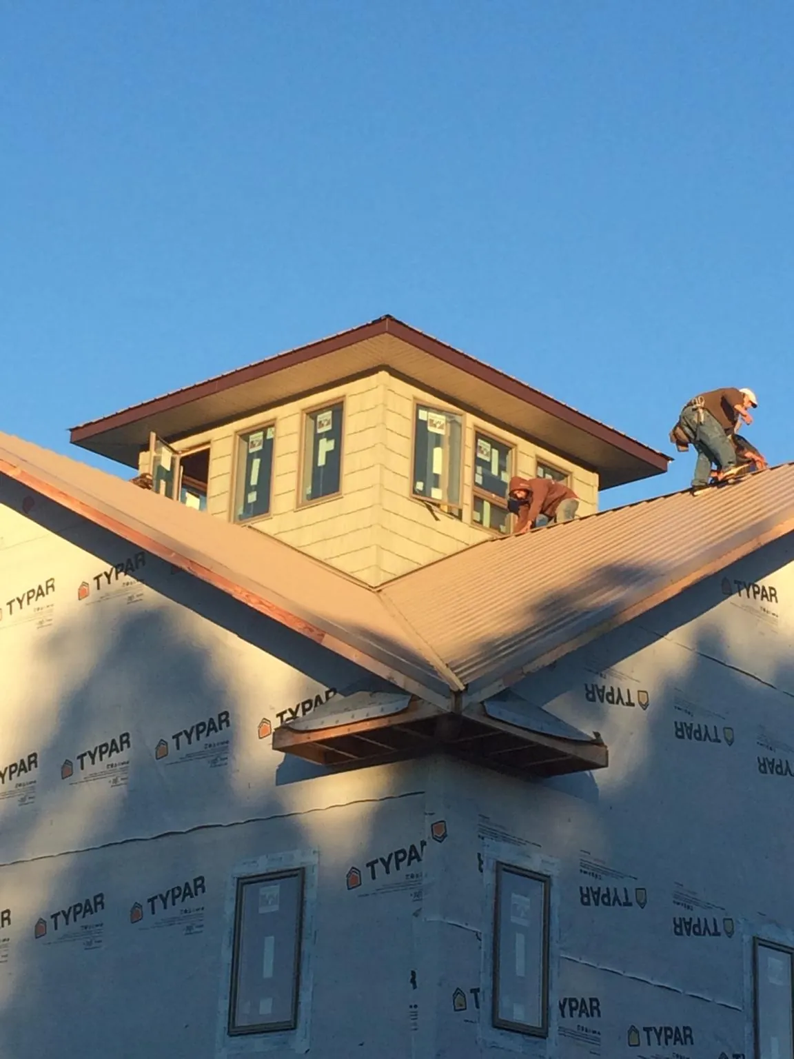 Roofers working around a rooftop cupola on a new metal roof at sunset — Roof Waterproofing in Chippewa Falls by Roofing Brothers